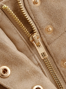 Detailed macro view of tan suede jacket featuring a metallic gold zipper and snap button