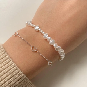Detail of layered sterling silver heart pendant bracelet and pearl bracelet on wrist