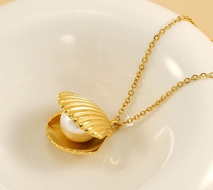 Detail of golden shell pendant necklace with white pearl on a ceramic plate