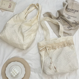 Detail of off-white pleated linen tote bags with lace trim and elegant tassel accents
