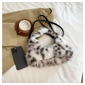 Flat lay of plush faux fur crescent bag with black spots on a white textured background