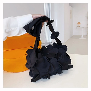 Detail of black 3D petal handbag made of premium fabric held by a model in a bright room