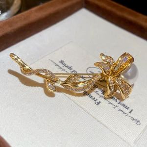 Macro shot of gold floral brooch with micro-pave zircons and a large white pearl detail