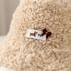 Close-up detail of a beige lamb wool winter hat with cute dog tag and velvet bow decoration