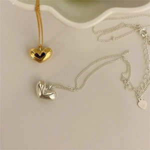 Detailed view of polished gold and silver heart necklaces on a ceramic tray