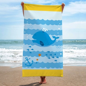 Blue microfiber beach towel with whale print shown on a sunny beach by a model