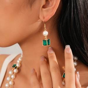Macro detail of gold earrings featuring white pearls and green cubic crystals on a model