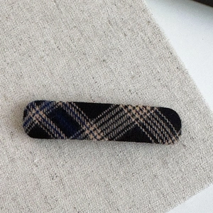 Detail view of a long rectangular hair clip with a blue and beige plaid tweed texture