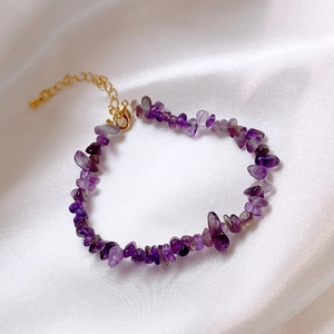 Dettaglio del bracciale in cristallo viola con chiusura dorata su seta bianca