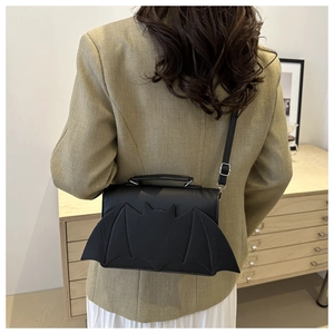 Rear view of a model wearing a unique black bat-shaped crossbody bag with a blazer