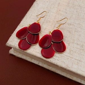 Detail of red tiered petal drop earrings with gold metal hooks on textured surface