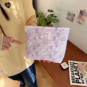 Detail of purple quilted cosmetic bag with cute floral patterns held by a model