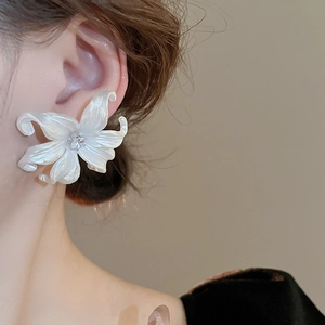 Detailed close-up of large white pearl acrylic flower earrings with crystal center on ear