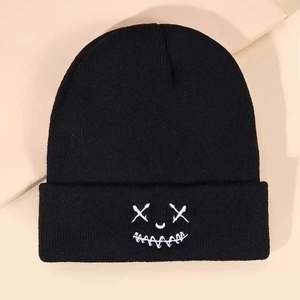 Close-up of black knitted beanie featuring white embroidered funny face design with X eyes