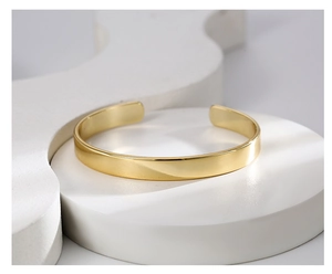 Detail of minimalist gold plated brass cuff bracelet on white geometric pedestal