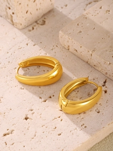 Macro detail of thick oval golden hoop earrings on a textured stone background