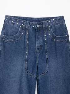 Détail d'un jean en denim bleu foncé avec des clous métalliques argentés à la taille