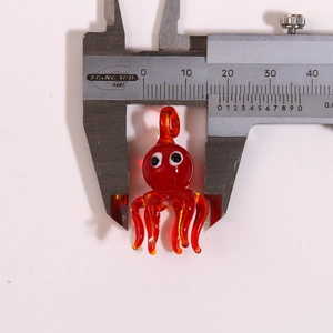 Macro shot of a red glass octopus pendant measured with a caliper showing 20mm width