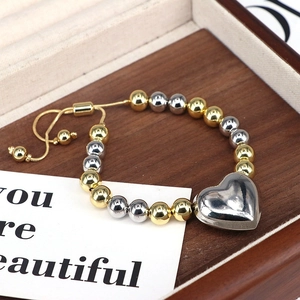 Bracciale regolabile a sfere bicolore con ciondolo a cuore argento su vassoio legno