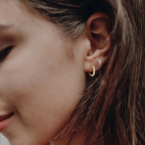 Close-up of a gold crystal hoop and silver lightning stud earring on a model