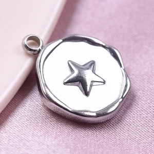 Macro shot of a silver irregular round pendant with a raised star on pink satin fabric