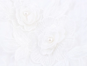 Detail of white lace fabric featuring 3D floral embroidery and elegant pearl accents