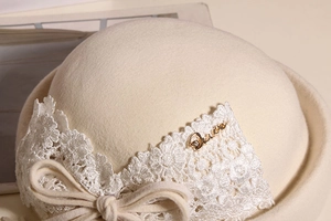 Detail of wool cloche hat with lace bow decoration and gold metal logo accent