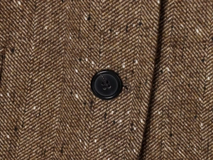 Close-up of brown herringbone tweed fabric texture with a classic black button