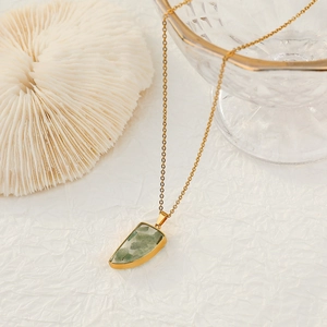 Elegant gold necklace featuring a green natural stone pendant on white textured background