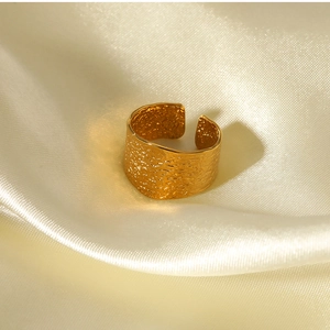 Detail of wide C-shape ring with hammered gold texture on elegant silk background