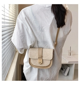 Detail of a woven straw saddle bag with white PU leather trim and metal magnetic clasp