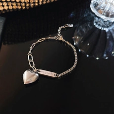Macro shot of S925 sterling silver asymmetric bracelet with heart pendant and engraved tag