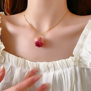 Close-up of a delicate gold chain necklace featuring a real pink rose bud pendant