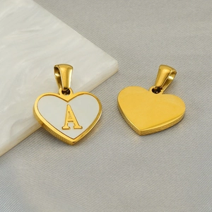 Polished gold heart pendant with letter A inlay on white marble and grey fabric background