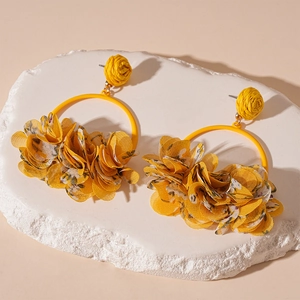 Detail of yellow fabric floral earrings with woven spheres and metal rings on a white stand