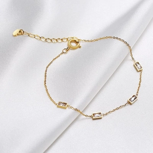 Detail of gold chain bracelet with four rectangular zircons and heart charm extension