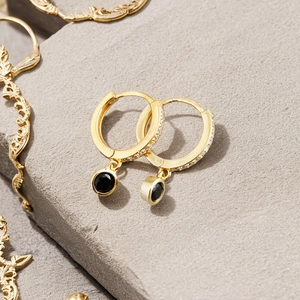 Macro shot of gold hoop earrings with black round charms on a grey textured background