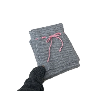 Grey knitted scarf with a pink bow detail held by a gloved hand on white background