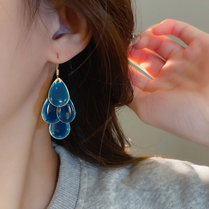 Close-up of a model wearing dark blue water-drop dangle earrings with gold metal trim