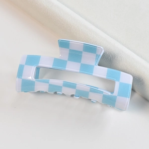 Detailed top view of a blue and white checkered acetate claw clip on neutral fabric