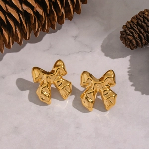 Macro shot of gold bow stud earrings with lava texture on marble with pinecones