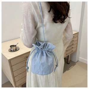 Close-up of light blue pleated bucket bag with drawstring and slender strap on a model