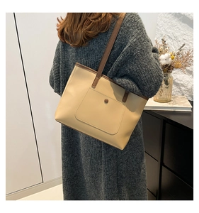 Close-up of beige tote bag with brown trim and front flap pocket on model's shoulder