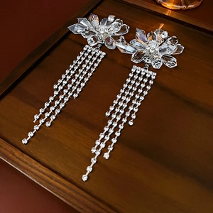 Detailed view of crystal flower earrings with silver rhinestone tassels on dark wood