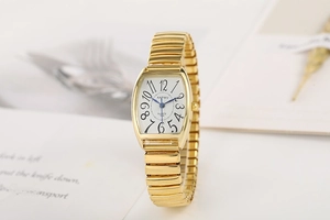 Détail d'une montre tonneau dorée à quartz avec grands chiffres et bracelet extensible