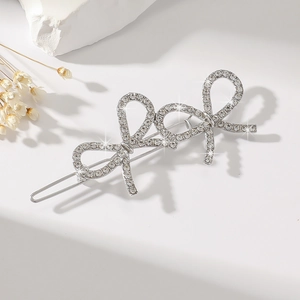 Detailed view of silver bow hair clips with rhinestones and pearls on a white stone surface