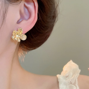 Macro shot of elegant golden flower stud earring worn, highlighting its metallic luster