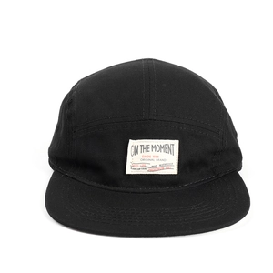 Dettaglio di un cappello 5-panel in tela nera con un logo vintage tessuto sul davanti