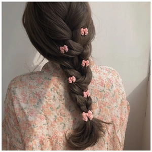 Six small matte pink bow hair clips used to decorate a girl's side braid hairstyle