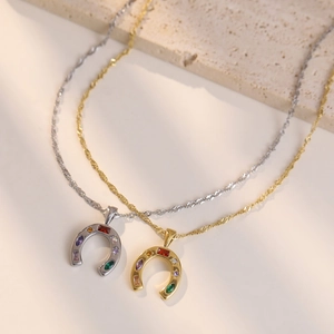 Gold and silver horseshoe necklaces with colorful zircon stones on stone surface